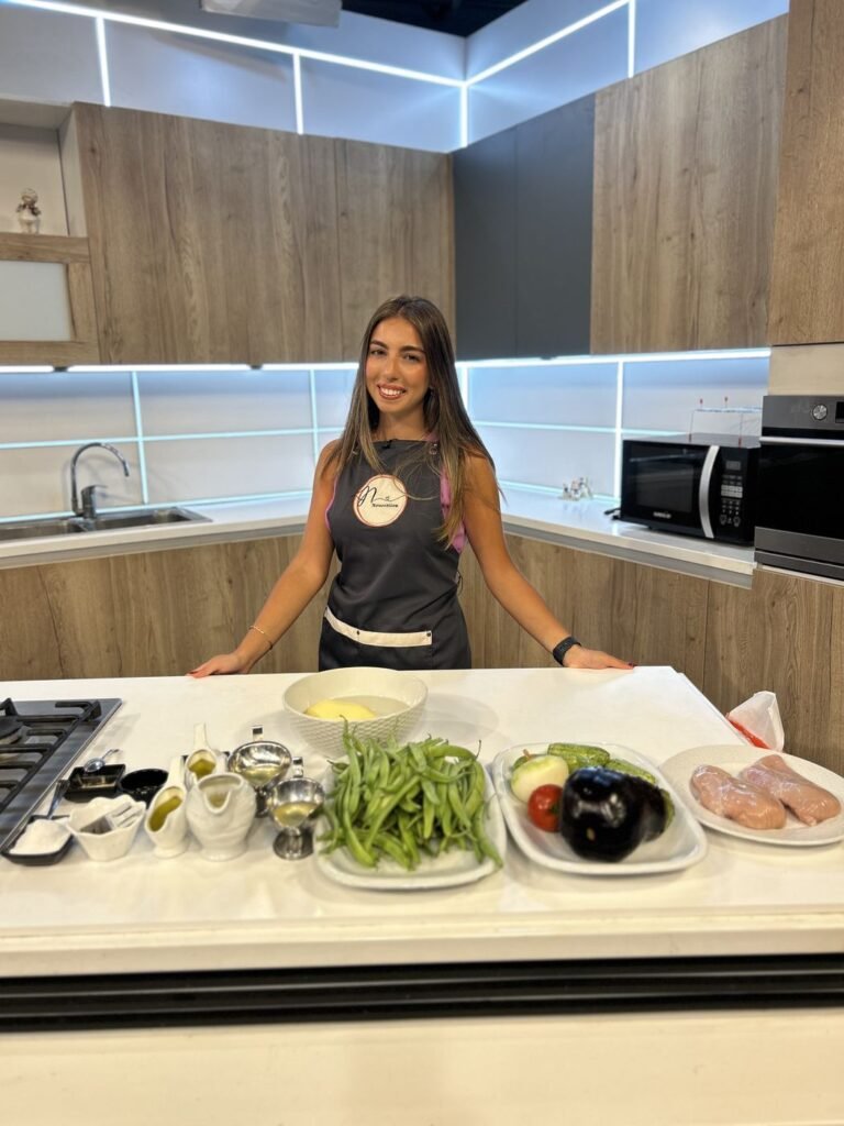 Nour, registered dietitian-nutritionist, smiling in a studio kitchen in her Nourrition apron, with green beans, vegetables and chicken on the counter